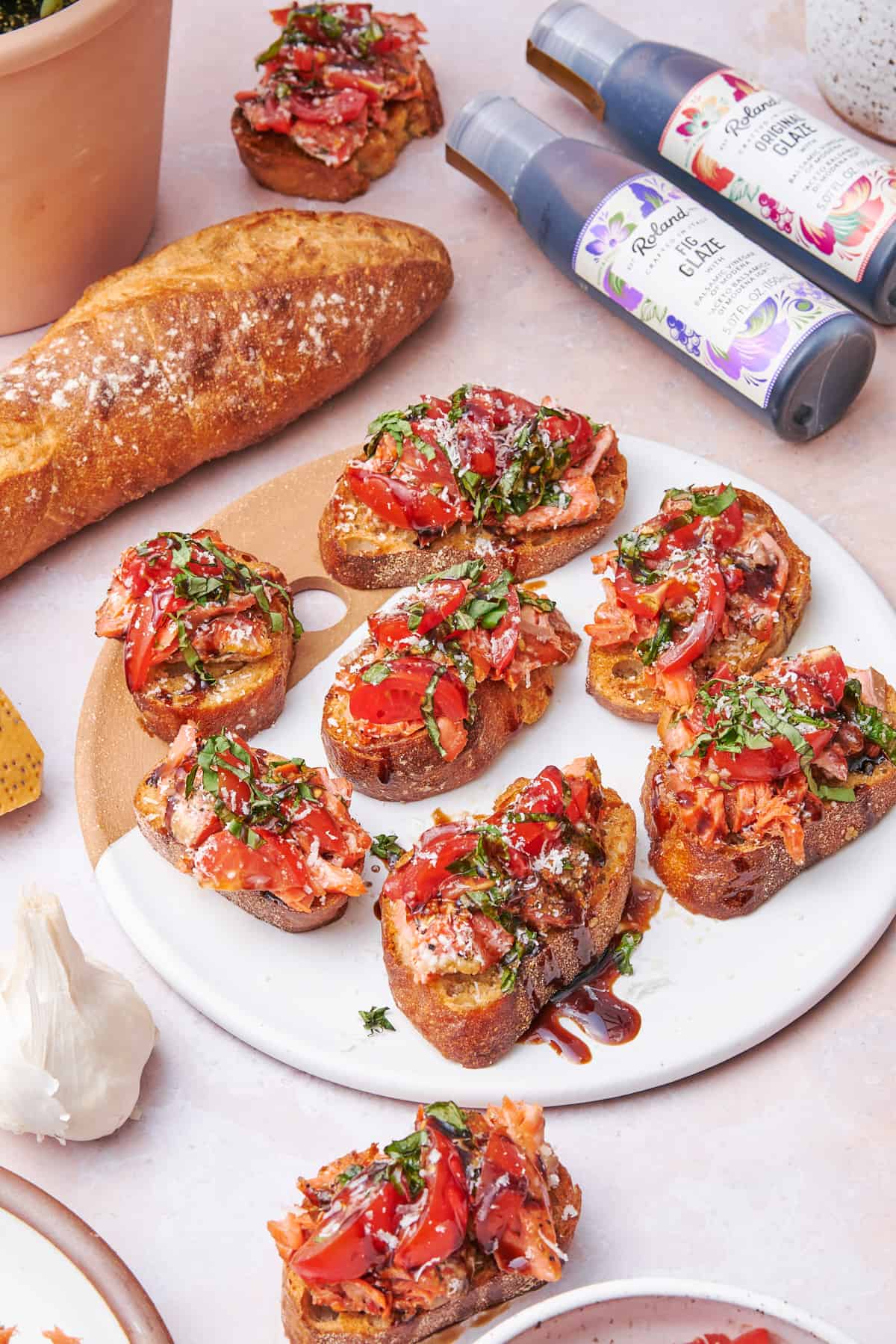 salmon bruschetta on a plate with bread, garlic, and roland balsamic glazes nearby.