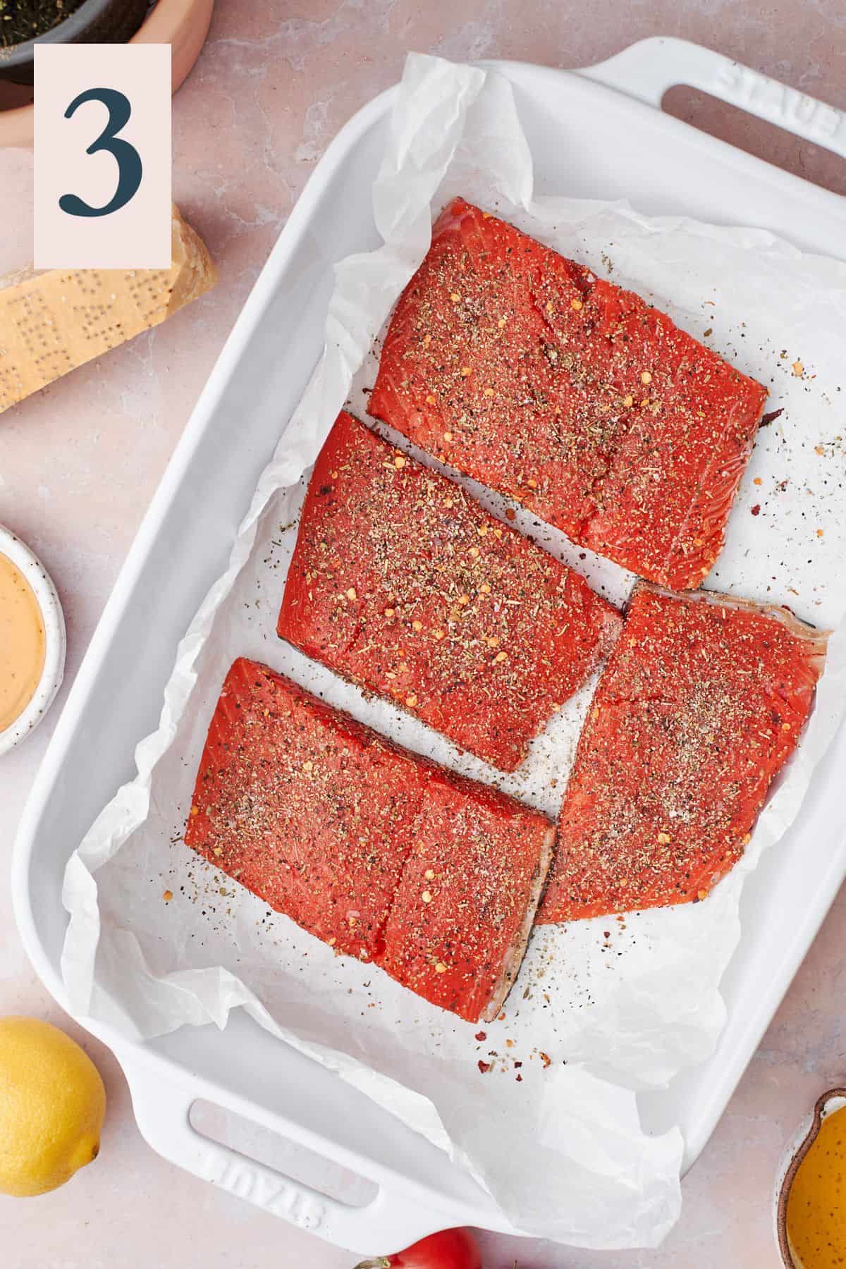 salmon fillets in a baking dish on parchment paper, seasoned very well.