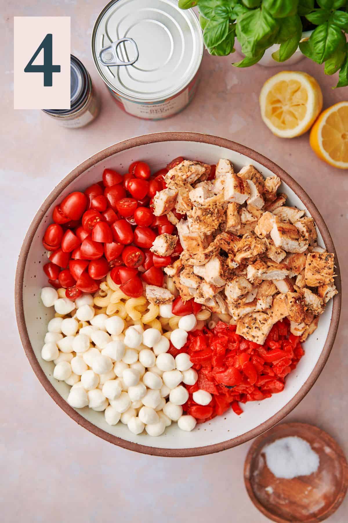 Large bowl with cooked pasta, cherry tomatoes, cut chicken, sliced red peppers, and mozzarella pearls.