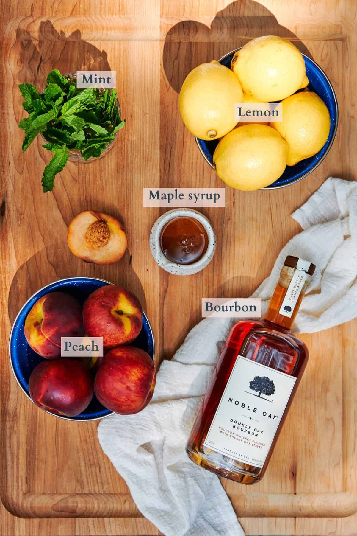 ingredients to make a peach bourbon smash laid out on a large cutting board labeled to denote each ingredient. 