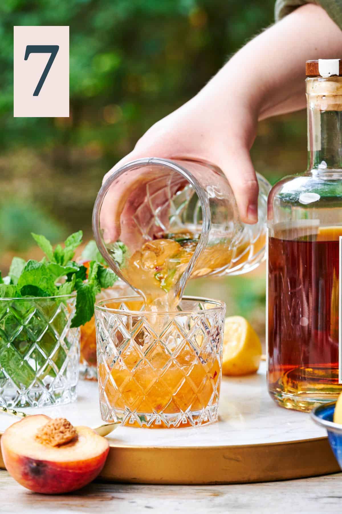 hand pouring a mixed peach drink straight from a mixing glass into a low ball glass. 