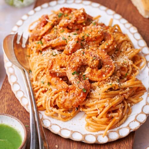 45-degree shot of spicy shrimp pasta on a platter with juicy shrimp and linguine, with green habanero sauce closeby.