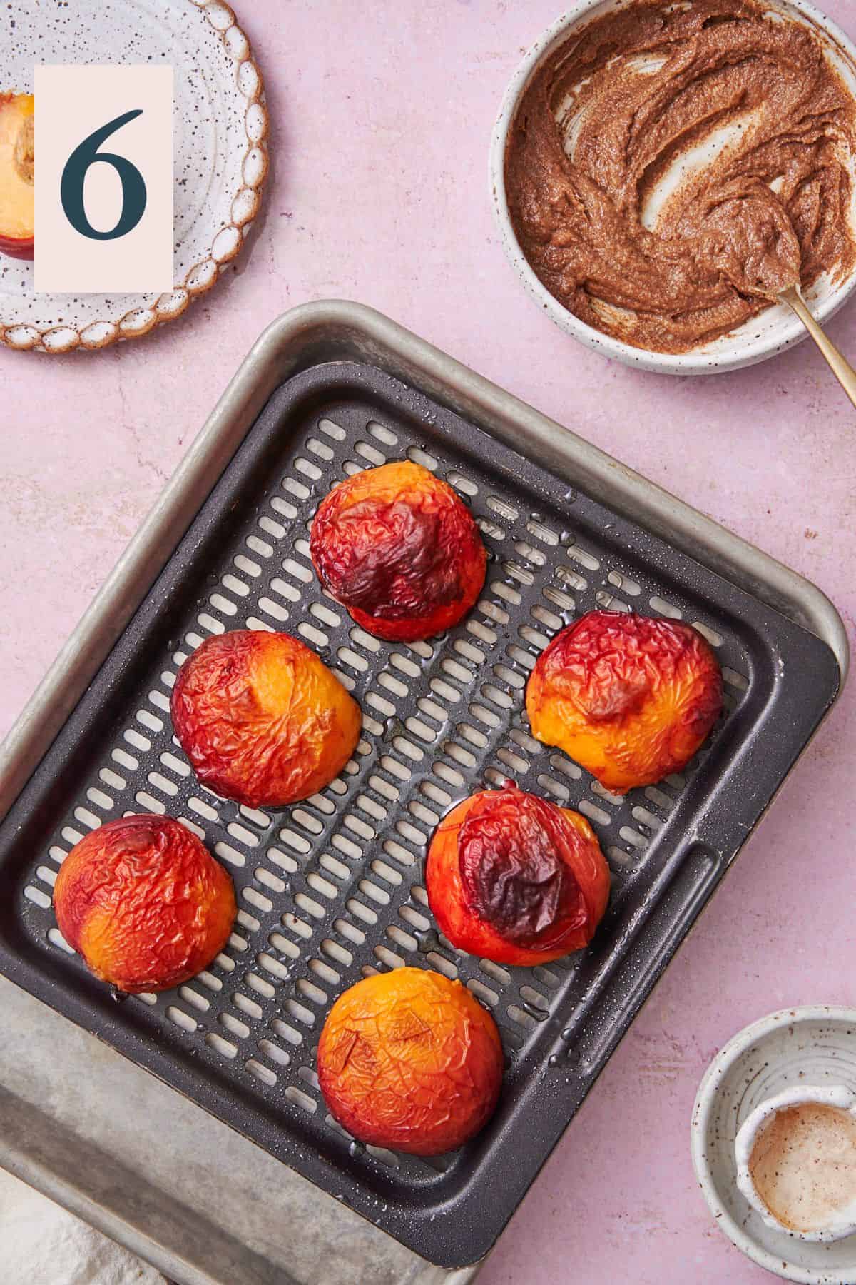 air fried peaches cut side down on an air fryer tray, cooked to soften with brown sugar cinnamon butter in a bowl nearby. 