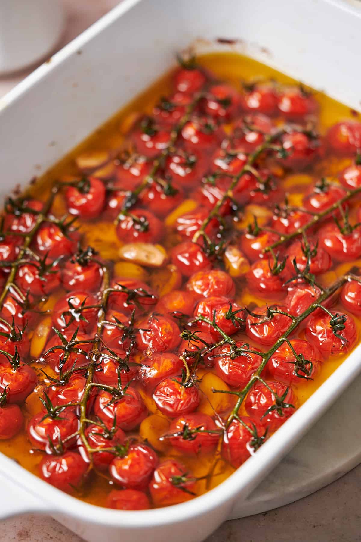white casserole dish with cherry tomatoes on the vine, with olive oil covering it and garlic. 