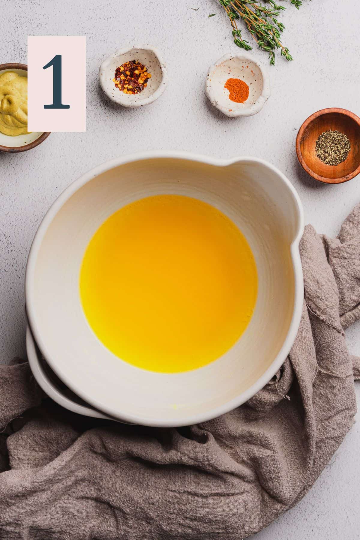 melted butter in a ceramic white mixing bowl surrounded by seasonings.