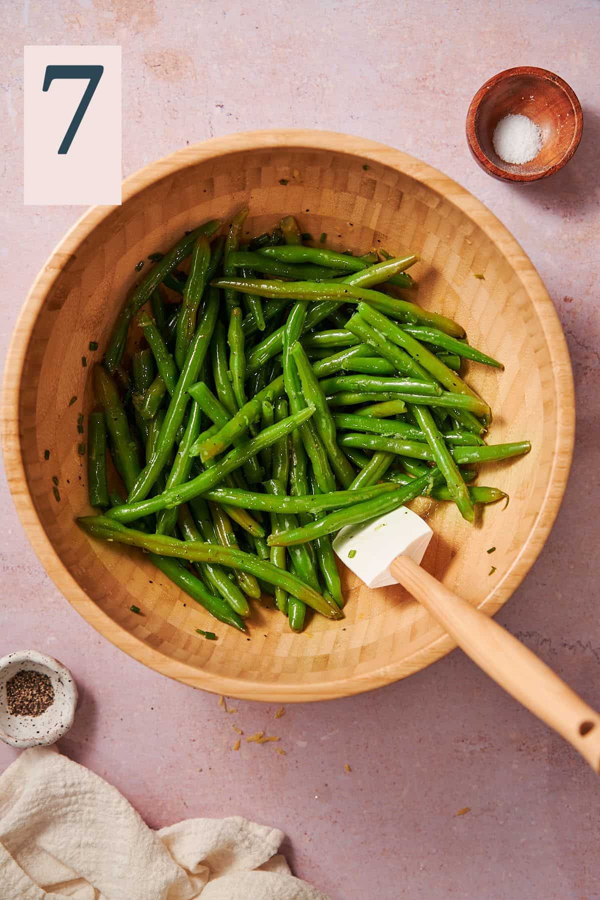 green beans in a large wooden bowl tossed with an olive oil dressing. 