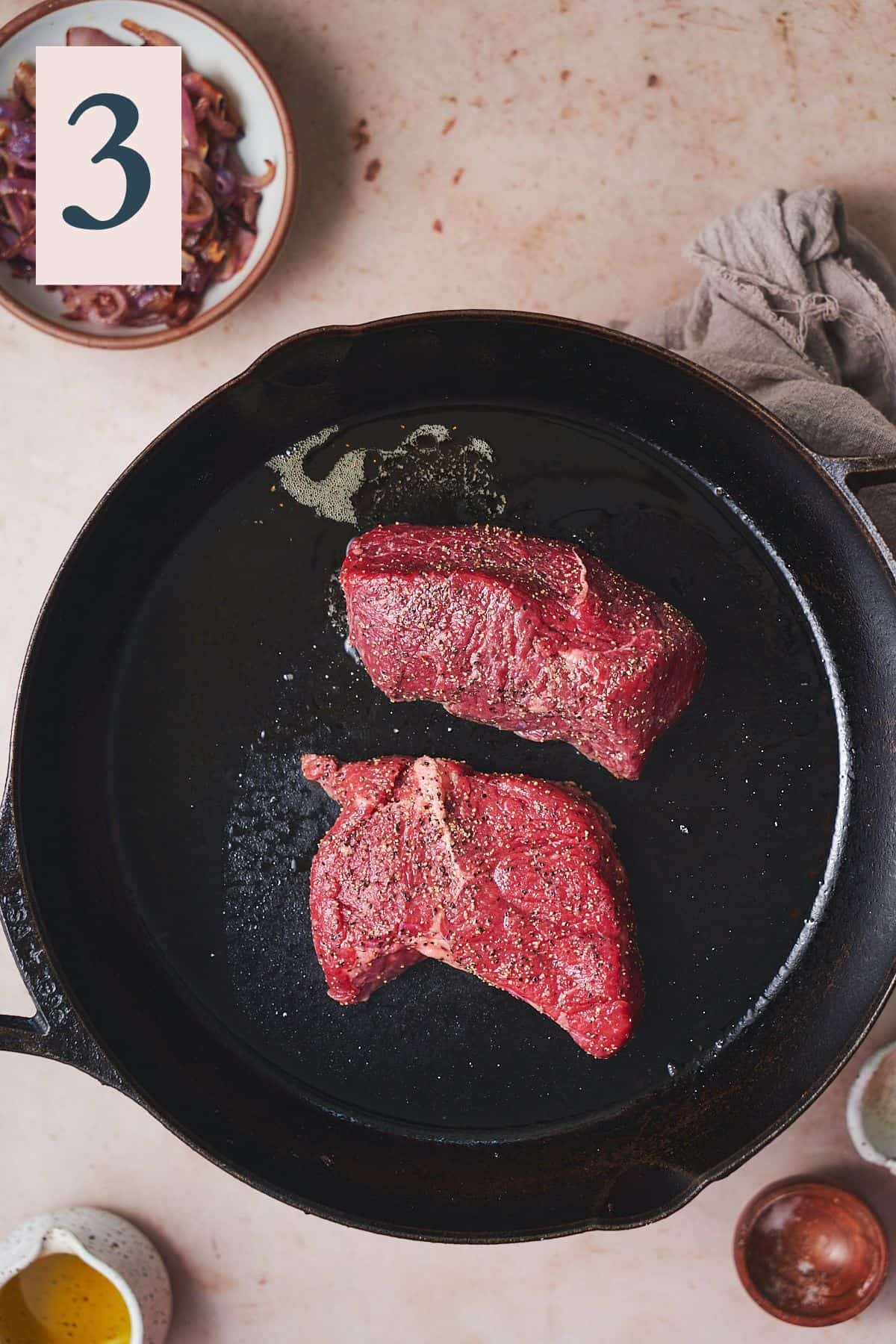 raw steaks seasoned with salt and pepper in a hot cast iron skillet.