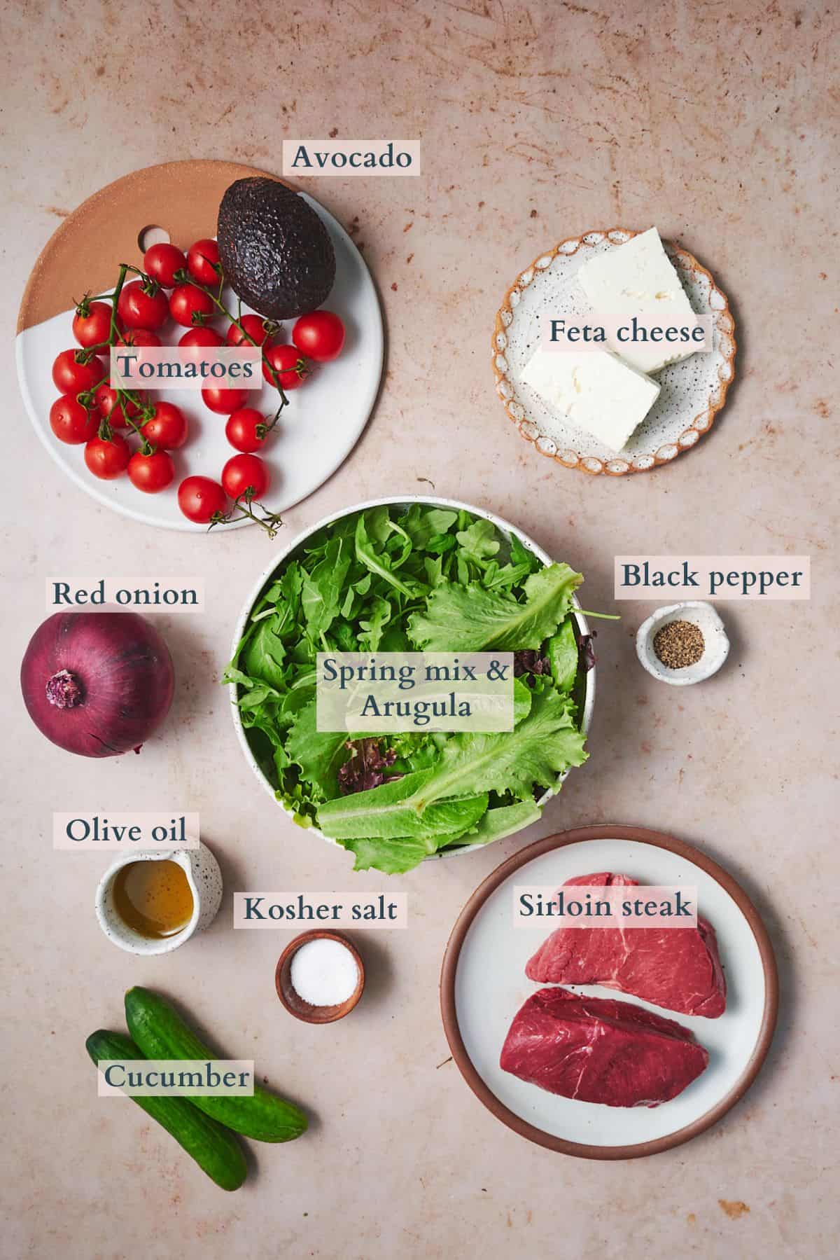 ingredients to make a steak salad laid out in bowls with text overlaying to denote each ingredient.