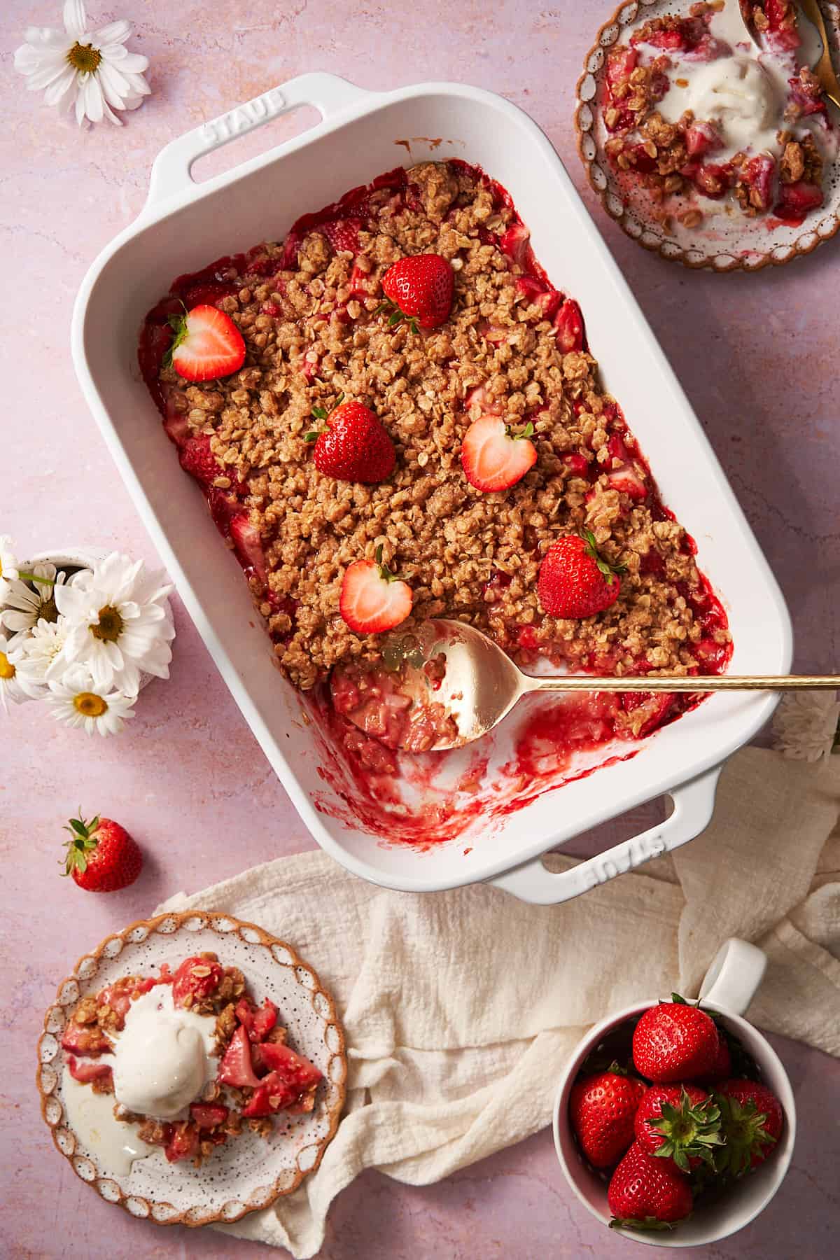 photo of a strawberry crumble in a large rectangular baking dish topped with fresh strawberries, and two plates near by topped with vanilla ice cream.  