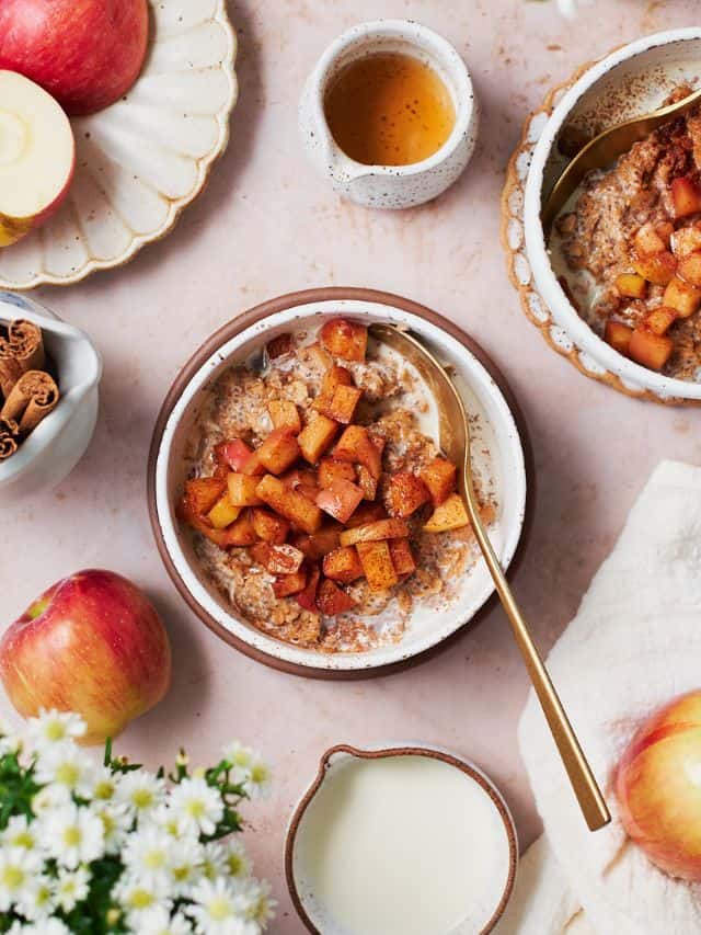 A bowl of apple cinnamon oatmeal topped with buttery spiced apples with small white flowers surrounding it.