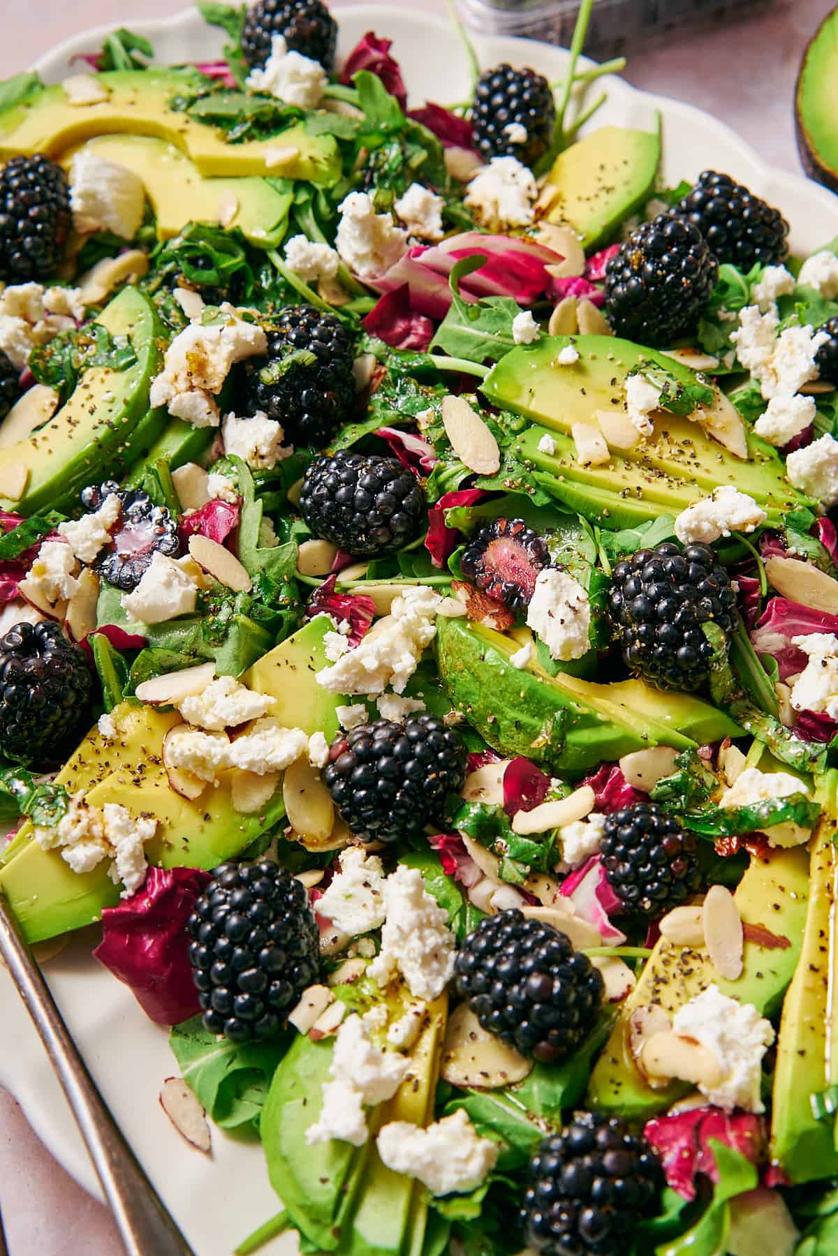 45-degree shot of a blackberry salad on a platter with goat cheese, almonds, avocado, arugula, and radicchio. 