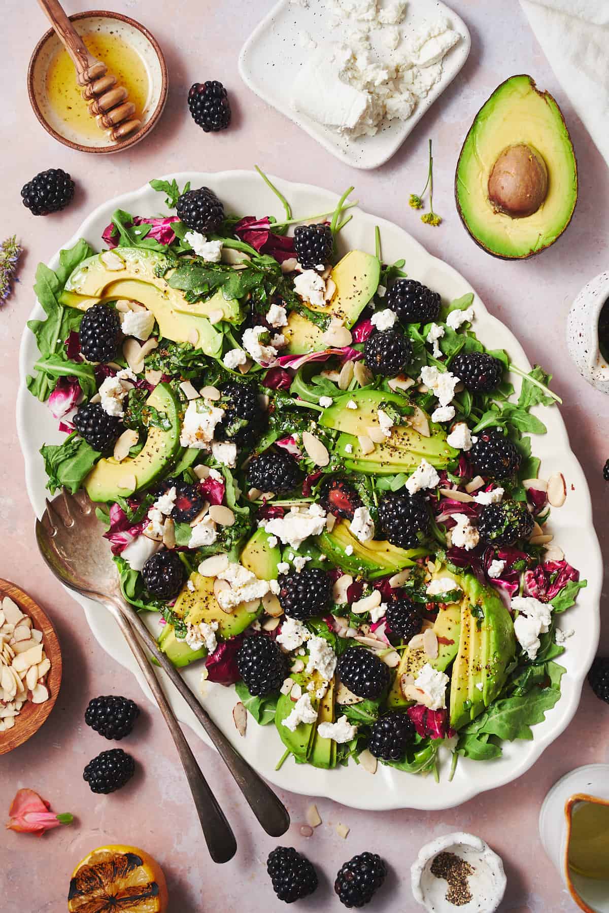 ruffled white salad plate with a blackberry and avocado salad, surrounded by lemons, blackberries, and crunchy almonds.