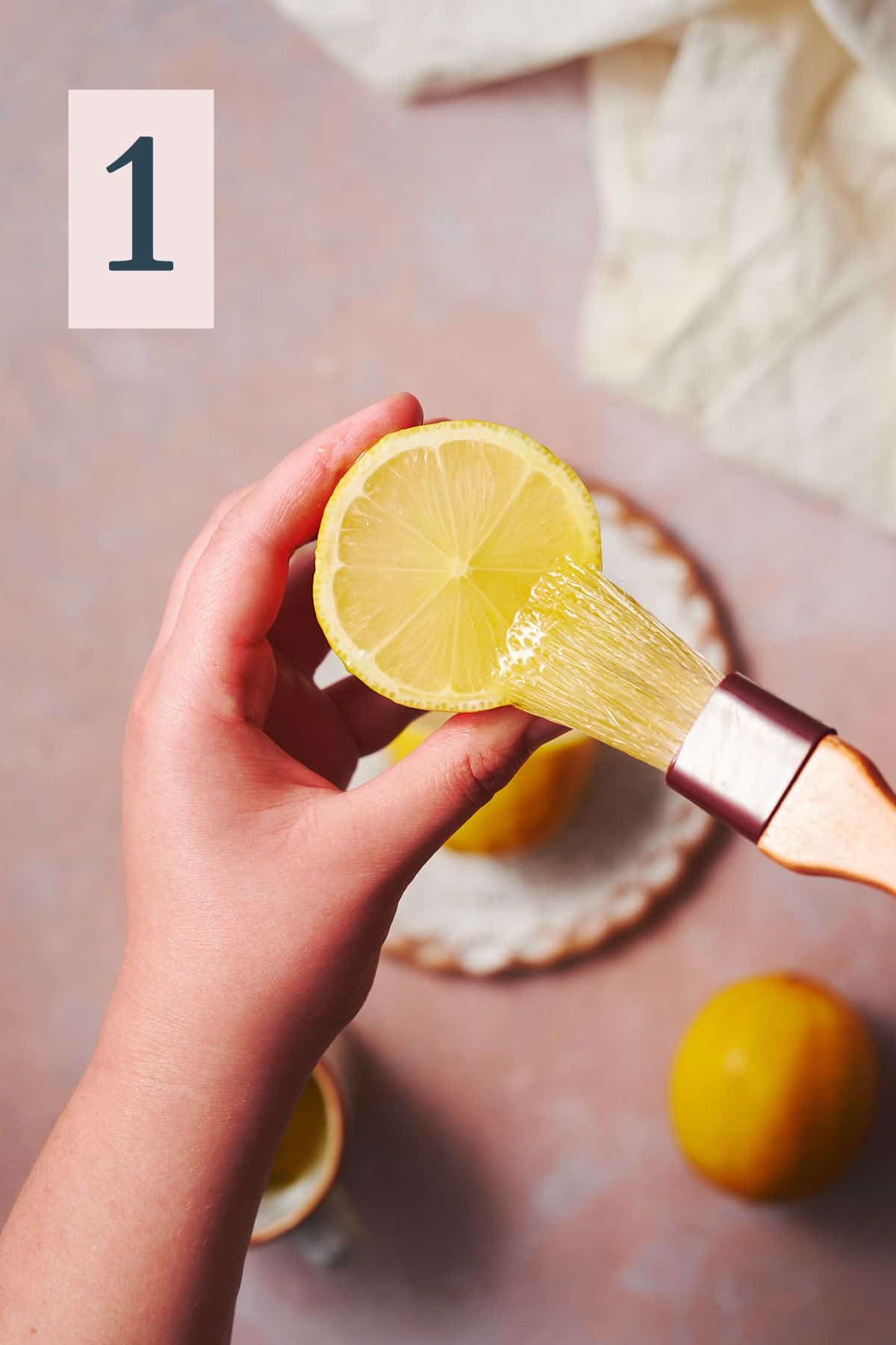 Hand brushing a half of a lemon with a pastry brush with olive oil. 
