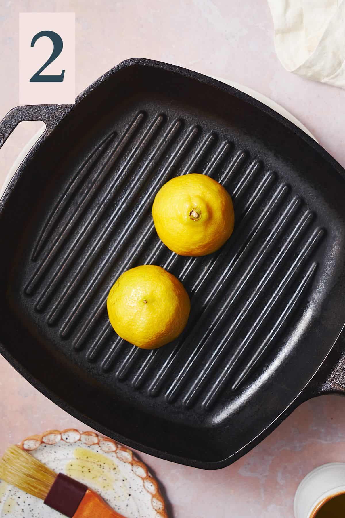 two lemon halves cut side down on a cast iron griddle pan grilling. 