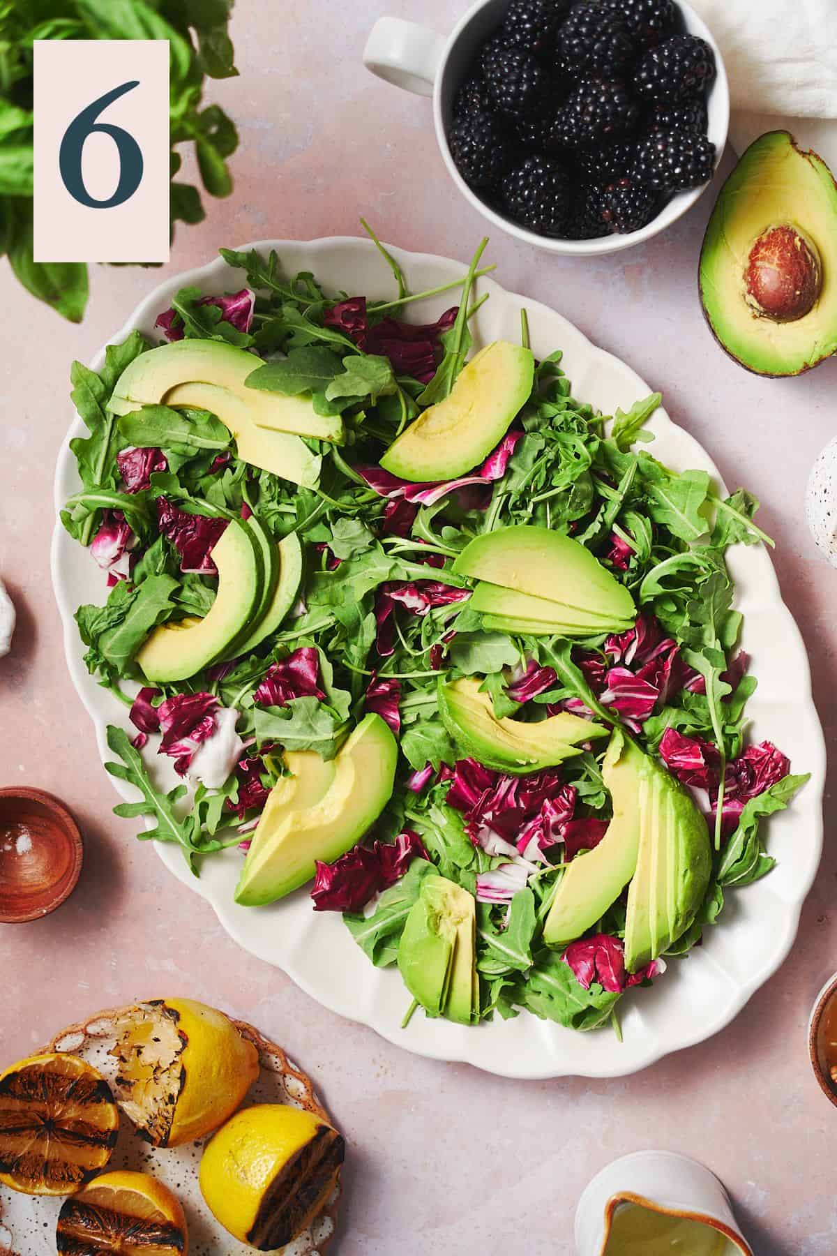 Arugula, radicchio, and avocado layered onto a ruffled plate surrounded by other ingredients to make a salad.  
