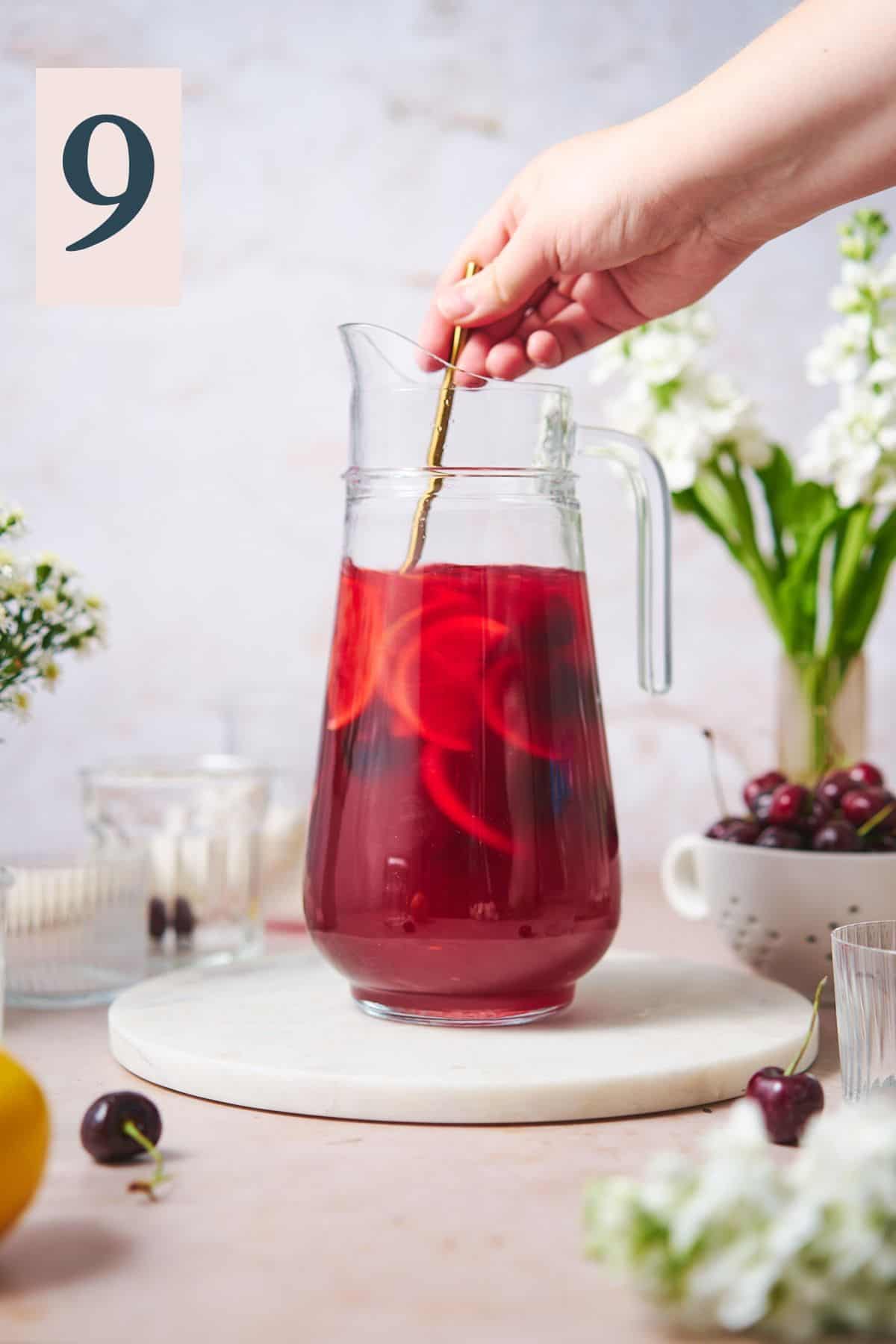 hand mixing a pitcher of cherry lemonade with a long spoon. 
