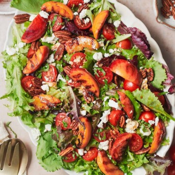 Grilled peaches salad on a scalloped plate with feta, cherry tomatoes, mixed greens, pecans, basil, and a vinaigrette.