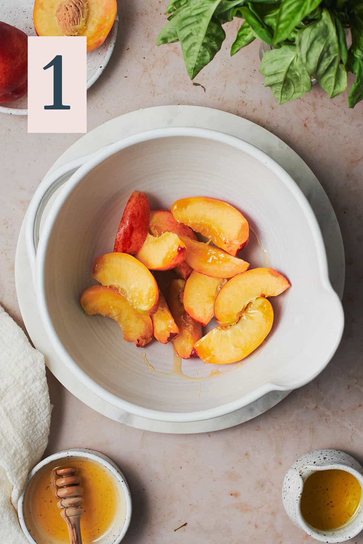 Sliced peaches in a ceramic bowl being tossed with honey and olive oil.