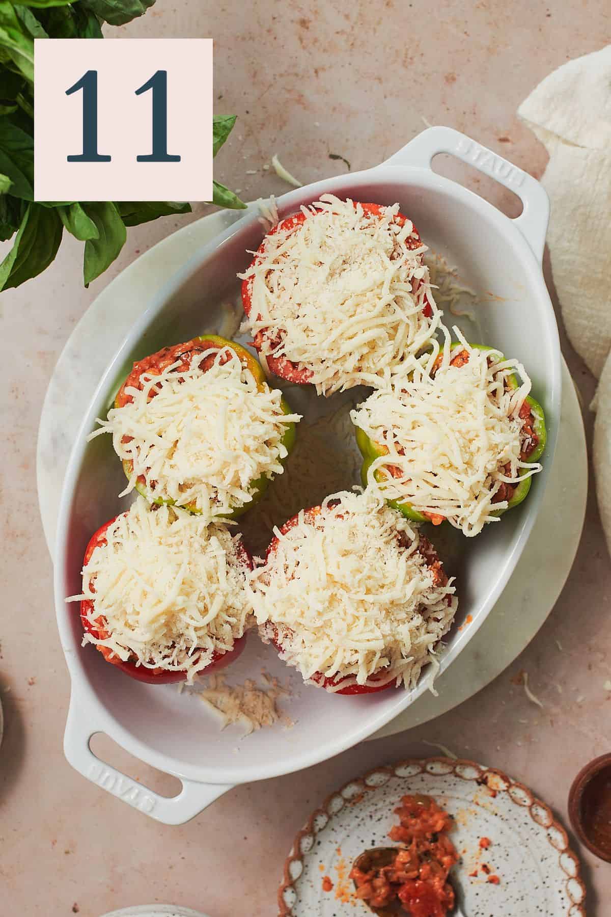 peppers topped with shredded cheese in a white oval baking dish. 
