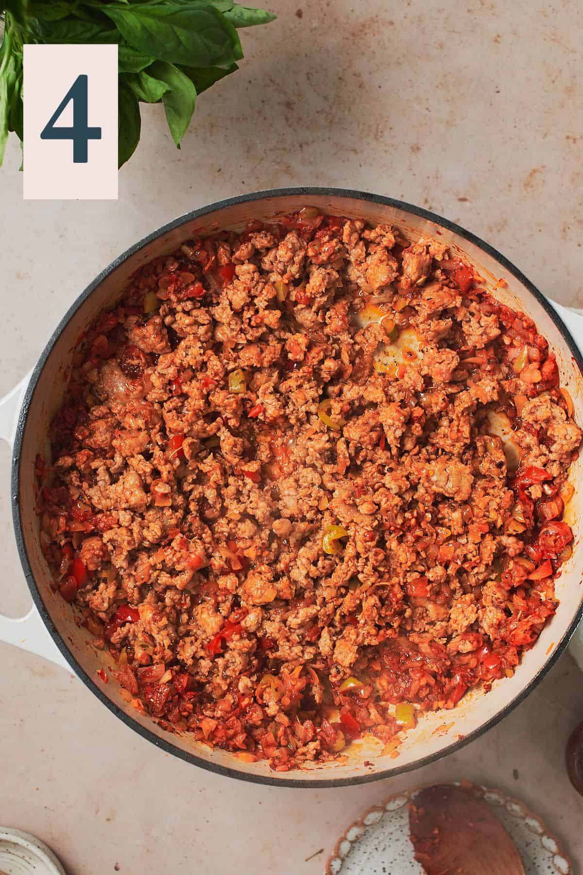 cooked Italian sausage crumbles in a skillet with tomato paste, seasonings, peppers, and onions. 