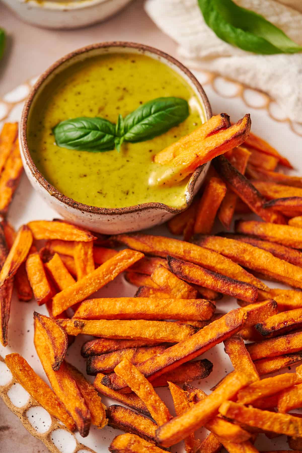 Pesto aioli in a ceramic pouring dish with sweet potato fries on a ruffled plate.