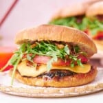 straight on shot of a juicy portobello mushroom burger with arugula, melty cheese, tomatoes, and caramelized onions.
