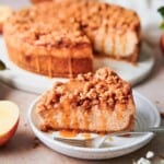 beautiful slice of apple crisp cheesecake taken out from a whole cheesecake in the back, with apples and salted caramel on the scene.