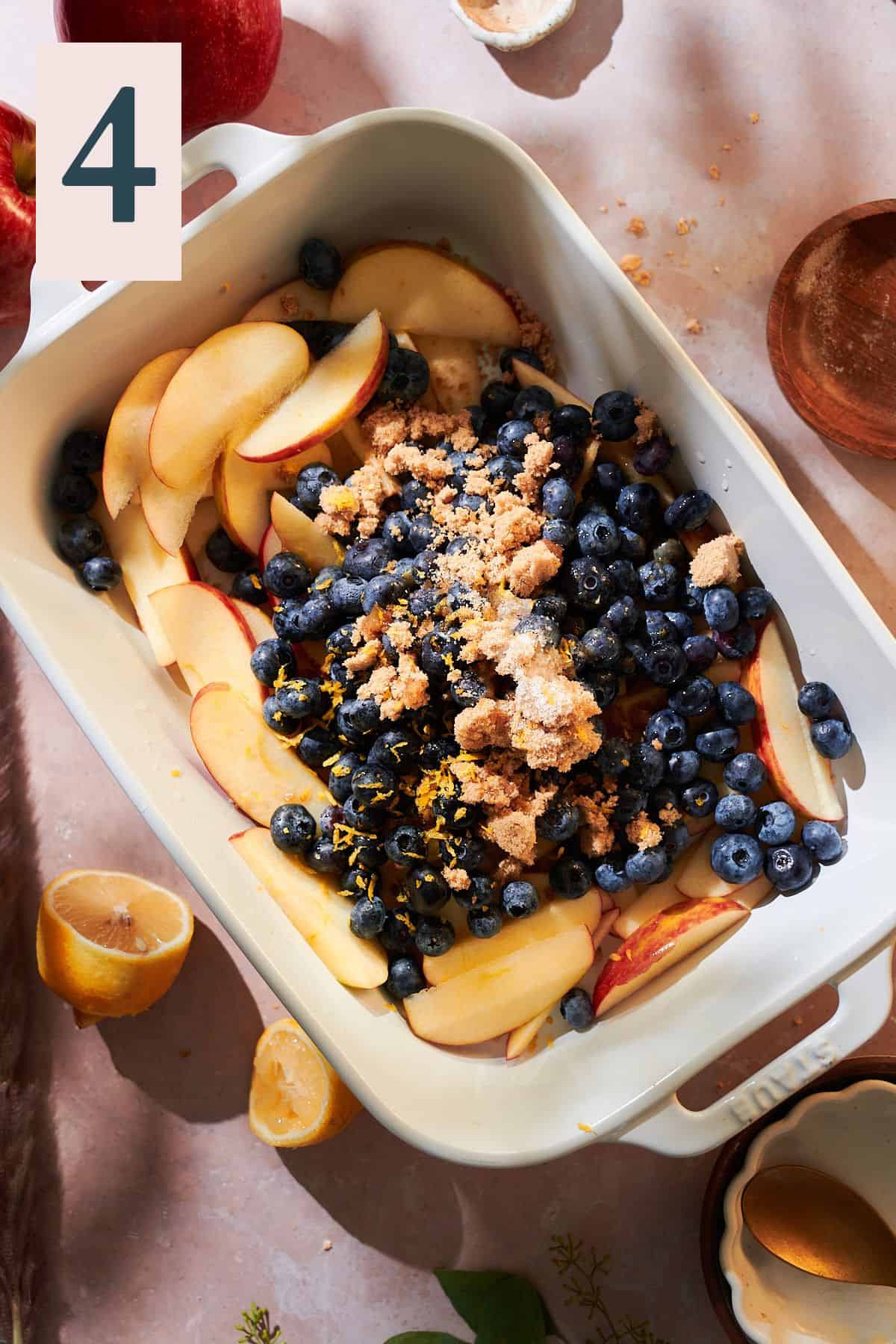 Apple slices and blueberries in a rectangular baking dish with brown sugar, cinnamon, lemon zest, lemon juice, brown sugar, salt, and vanilla extract. 