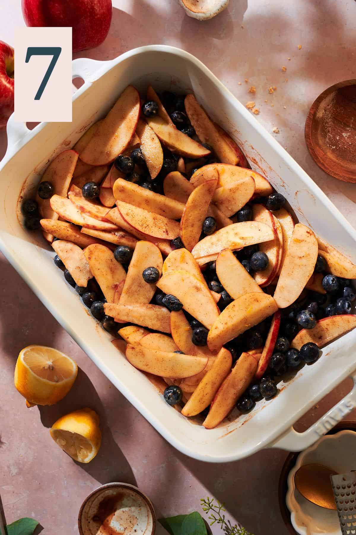 Apple slices and blueberries in baking dish with cinnamon, brown sugar, and lemons. 
