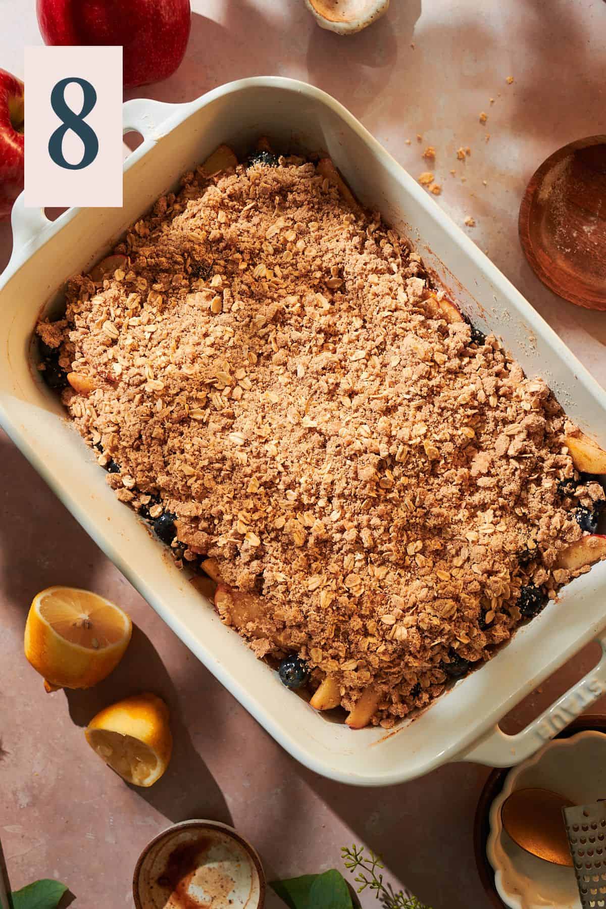 Crispy oat topping covering blueberries and apples in a baking dish before baking. 