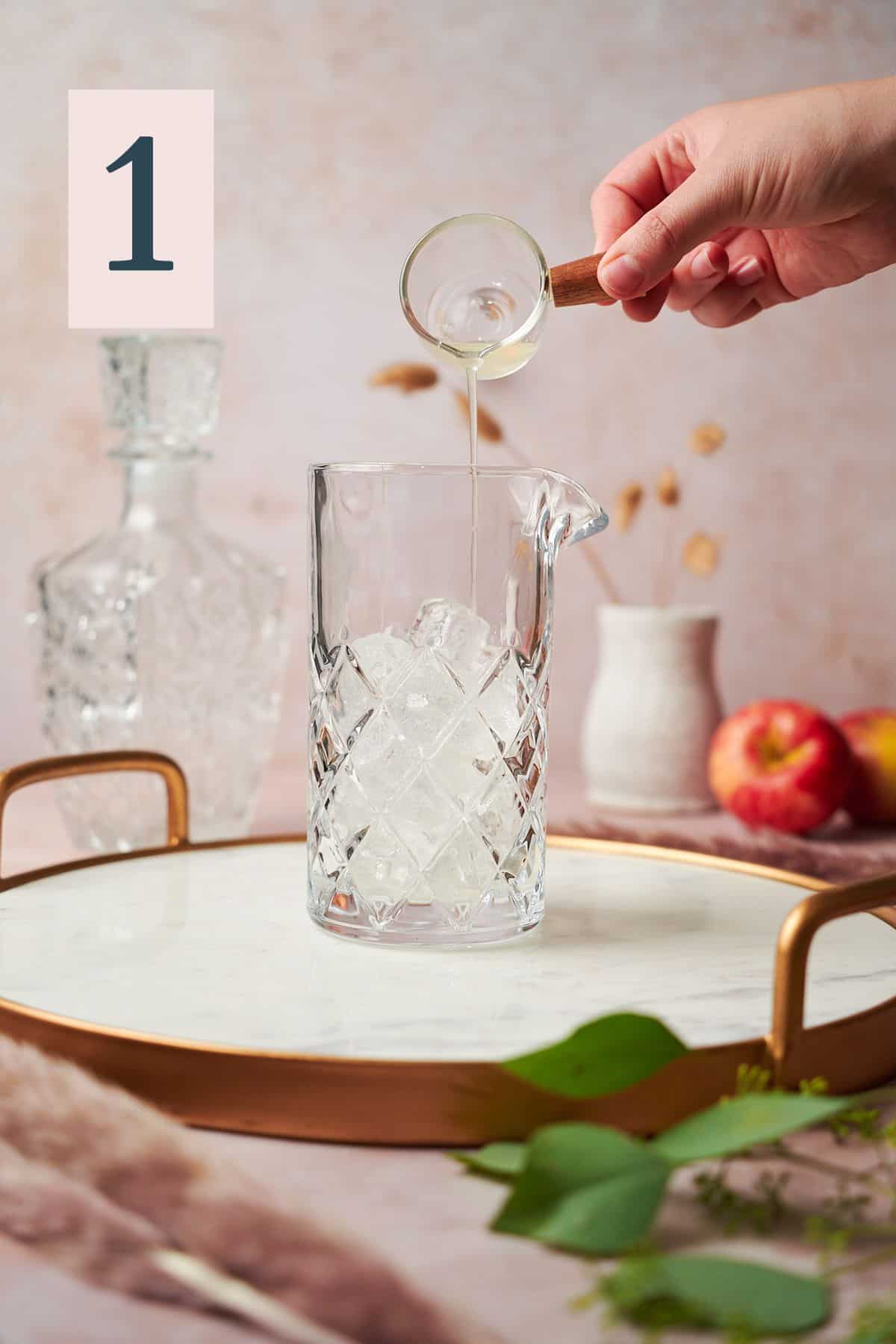 Hand pouring lemon juice into a mixing glass with pampas grass and apples in the background. 