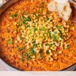 Close up shot of a cheesy corn dip topped with grilled corn, parsley, and green onions with bread dipped in.