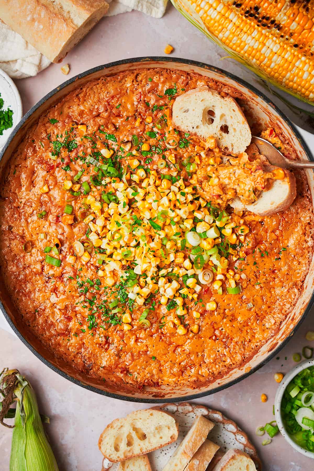 Corn dip recipe topped with green corn and green onions with bread slices inside of the dip. 