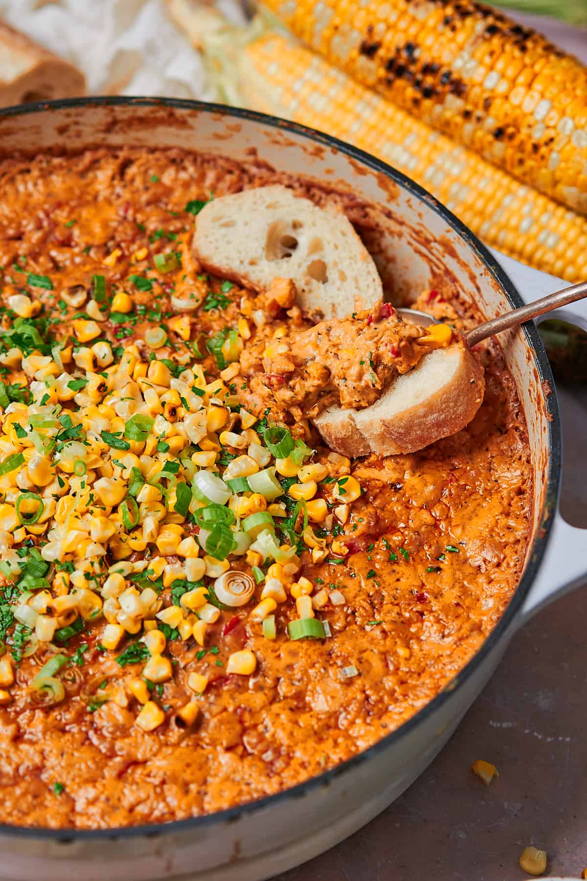 Close up shot of a cheesy corn dip topped with grilled corn, parsley, and green onions with bread dipped in. 