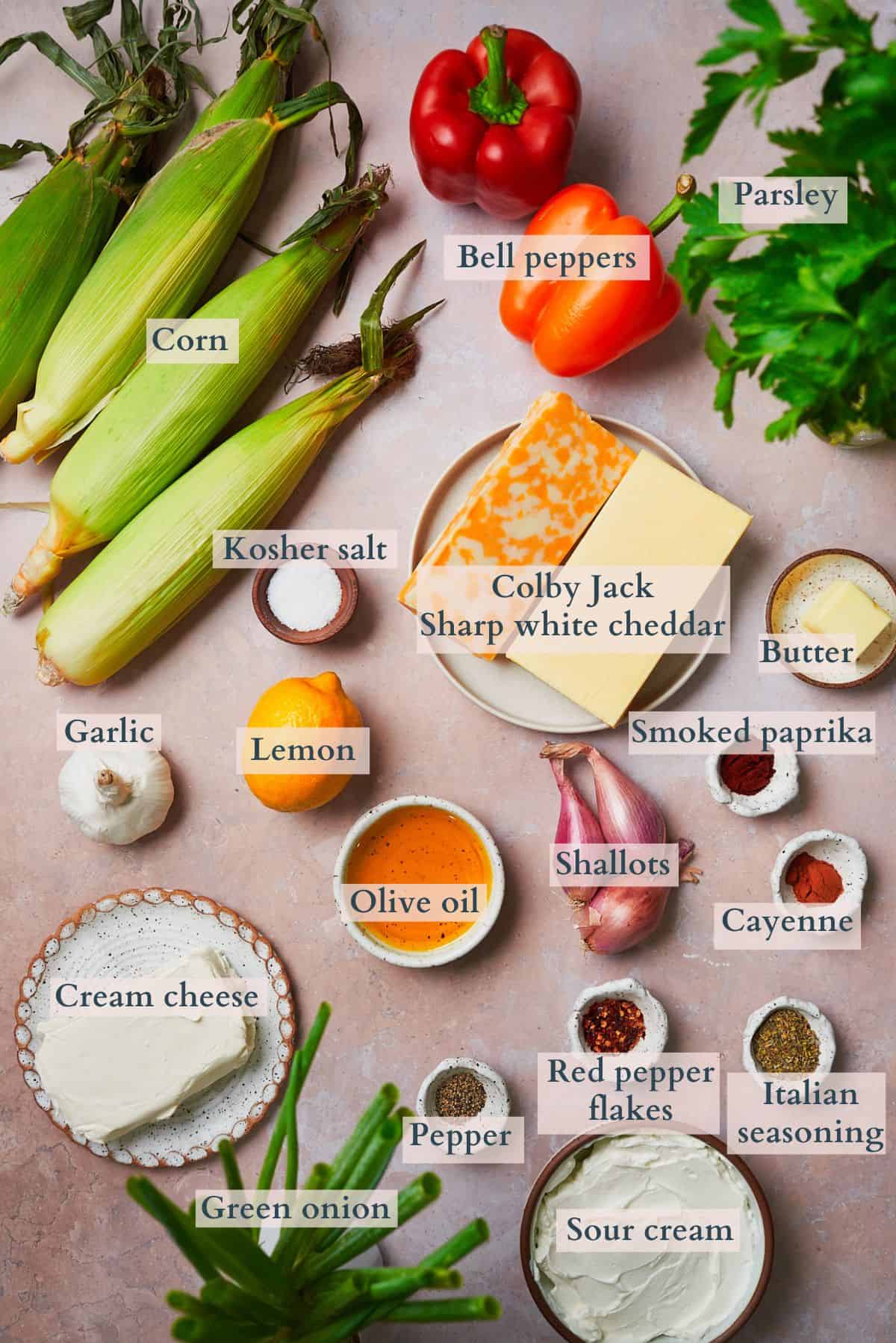 Ingredients to make a cheesy corn dip laid out on a table in small bowls and on plates, labeled to denote each ingredient.
