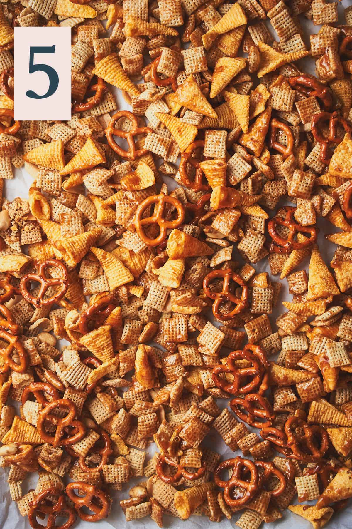 Cooked snack mix with pretzels, bugles, peanuts, and chex on a baking sheet. 