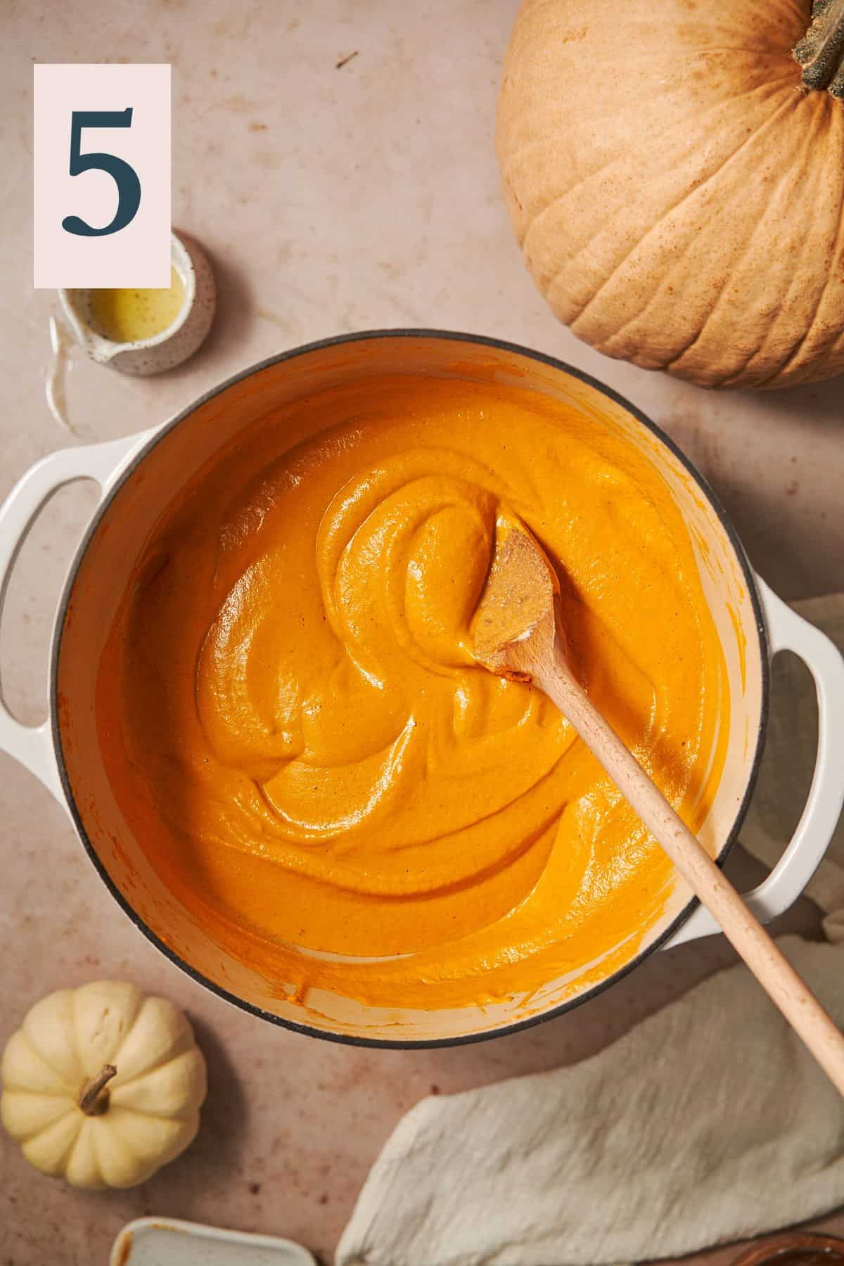 silky smooth pumpkin sauce in an enameled dutch oven with a wooden spoon stirring it until smooth. 