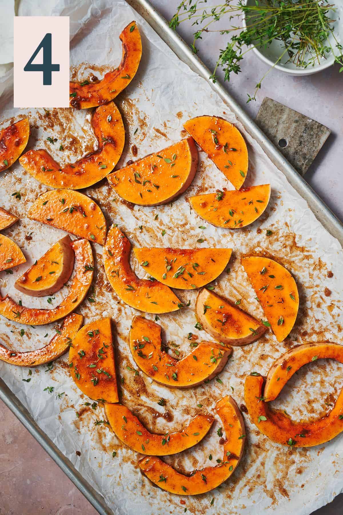 seasoned butternut squash pieces on a parchment lined baking sheet with thyme and other warm spices.