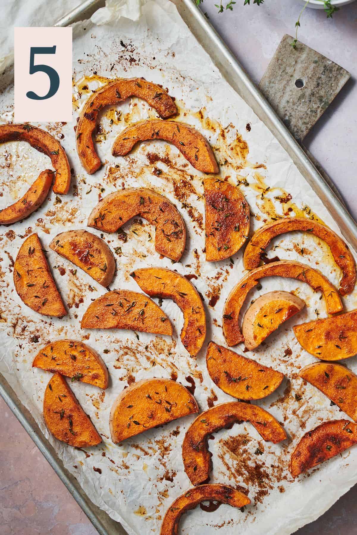 Roasted butternut squash pieces on a parchment lined baking sheet with thyme and cinnamon.