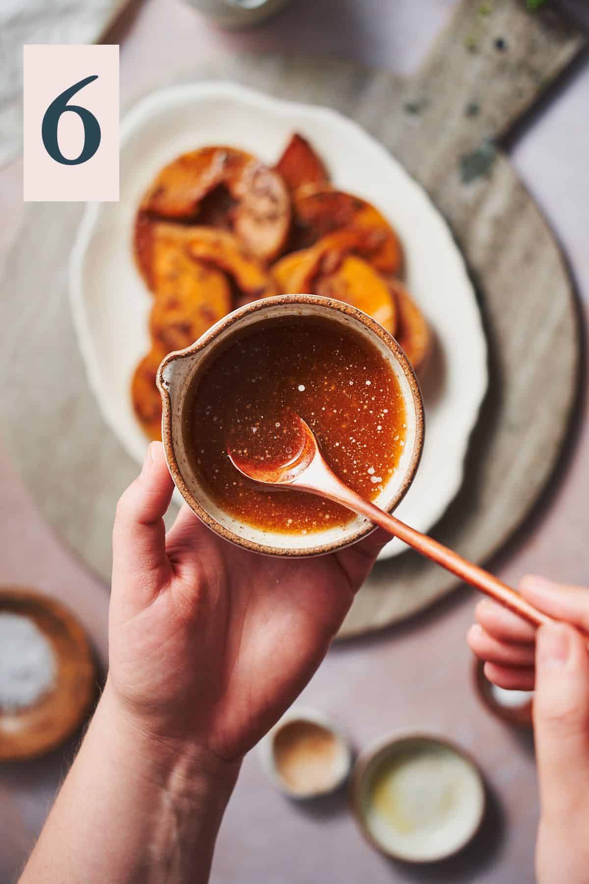hand stirring maple butter with cinnamon in a small bowl overtop of roasted squash. 