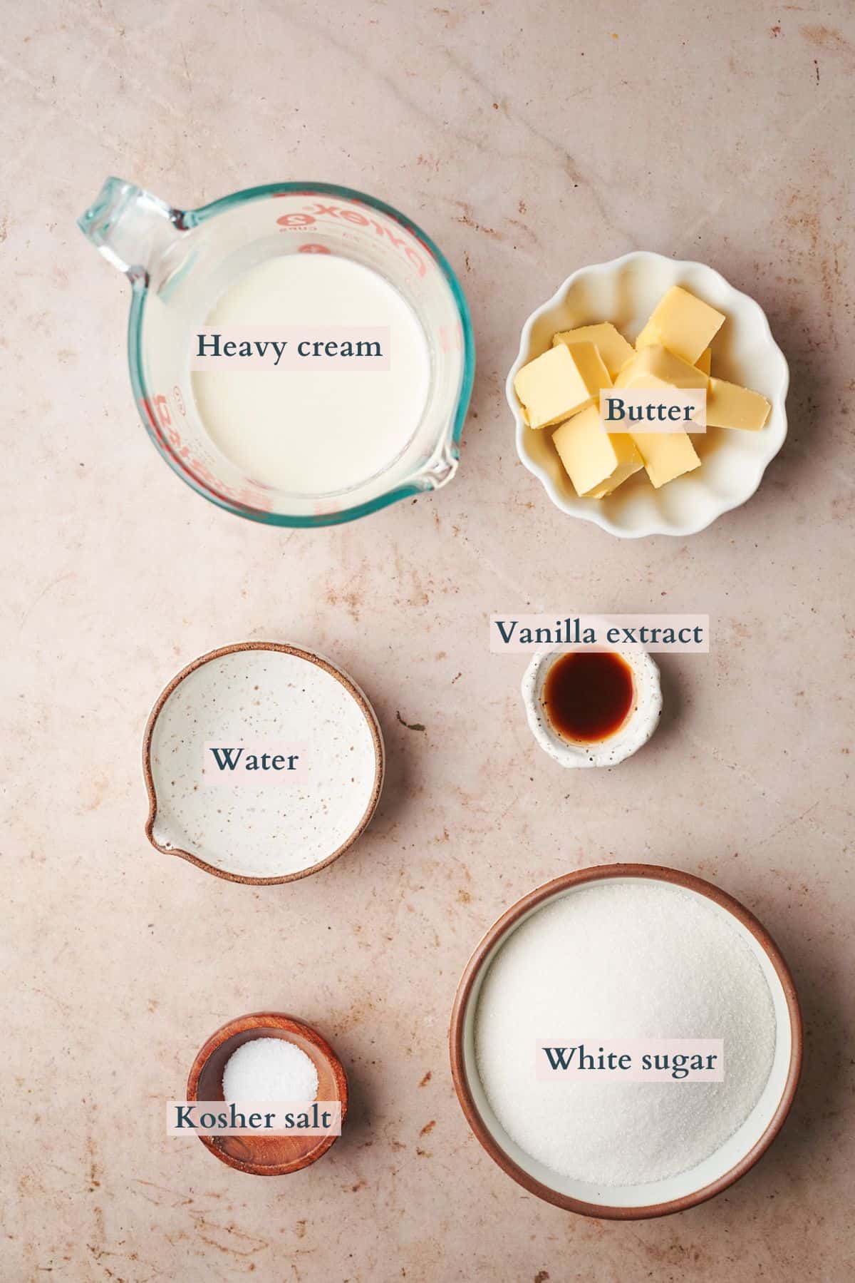 Ingredients to make salted caramel laid out in small bowls on a table labeled to denote each ingredient.