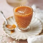 ornate glass jar with a spout full of slated caramel sauce on a ruffled plates, with a spoonful of caramel next to it.