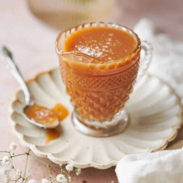 ornate glass jar with a spout full of slated caramel sauce on a ruffled plates, with a spoonful of caramel next to it.