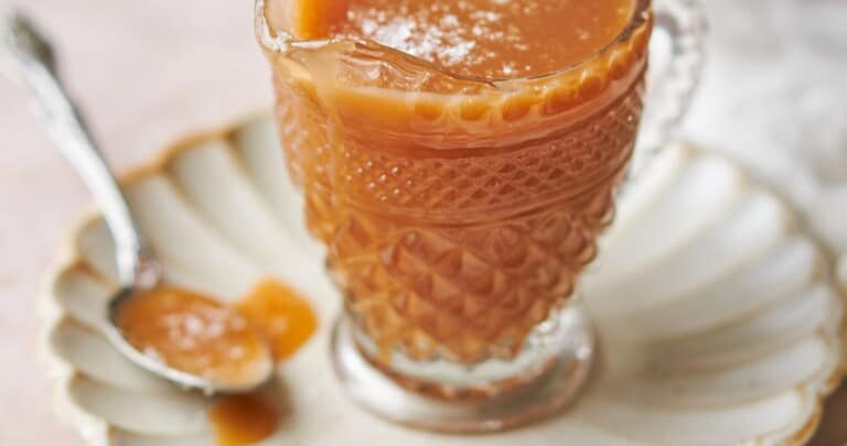 ornate glass jar with a spout full of slated caramel sauce on a ruffled plates, with a spoonful of caramel next to it.