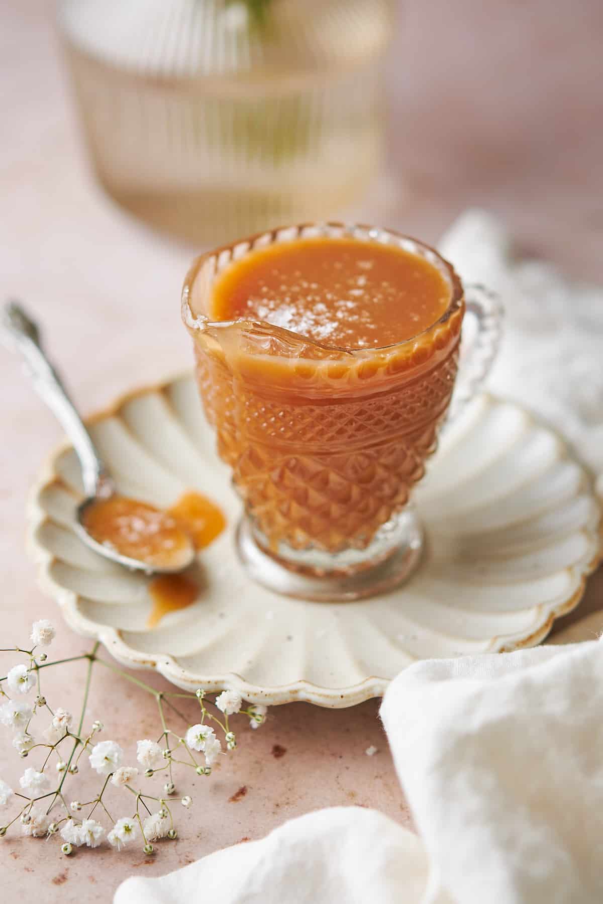 ornate glass jar with a spout full of slated caramel sauce on a ruffled plates, with a spoonful of caramel next to it. 