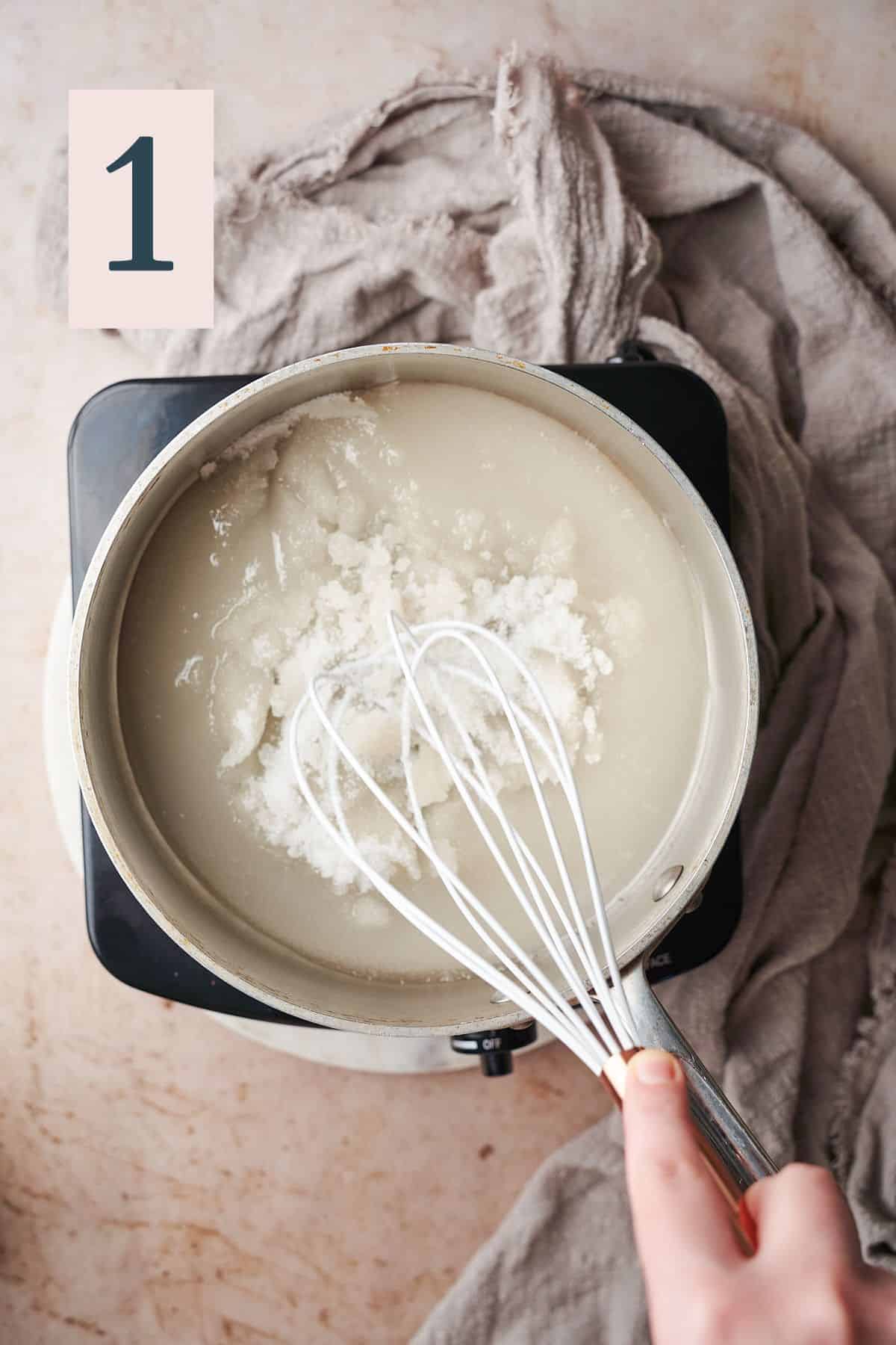 hand gently pushing a silicone whisk around a saucepan with sugar and water in it. 