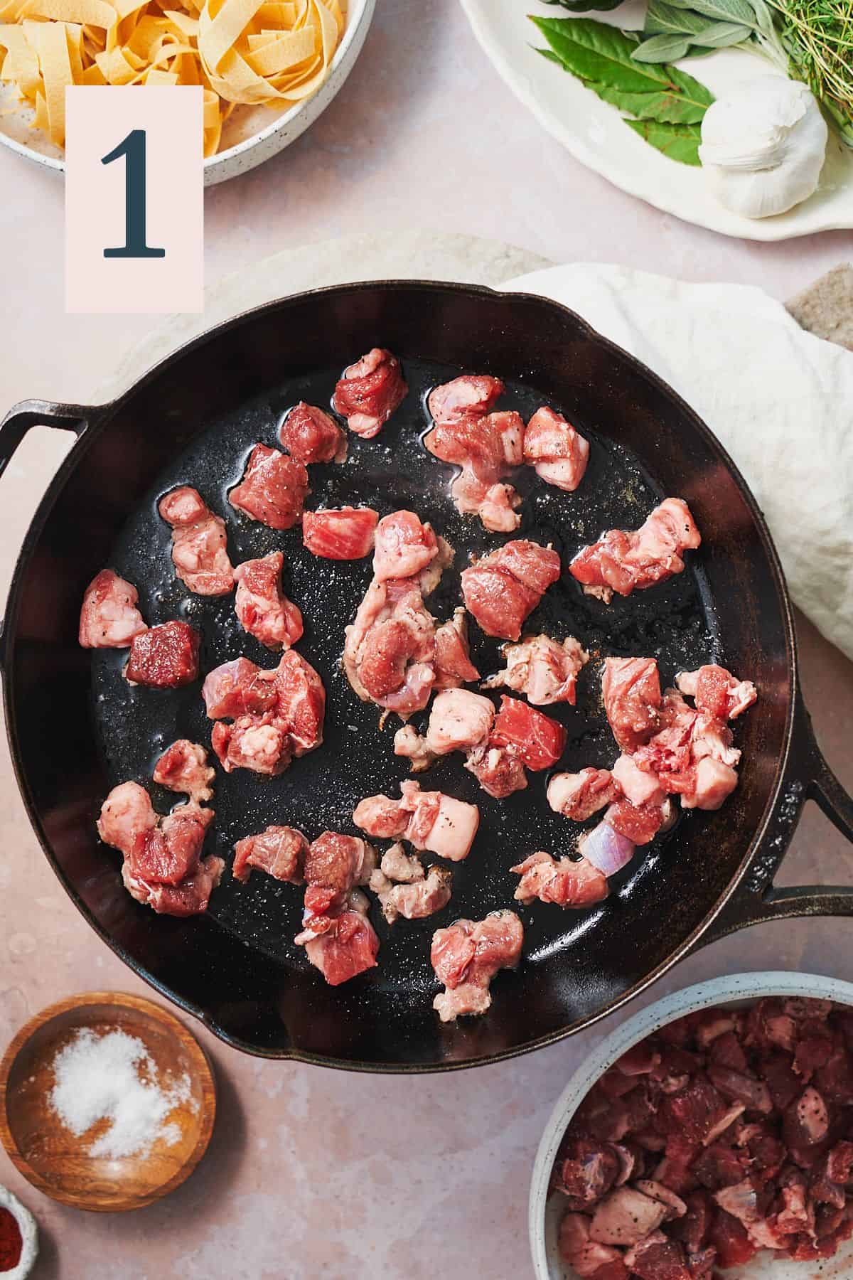 Raw chunks of lamb meat in a cast iron skillet.