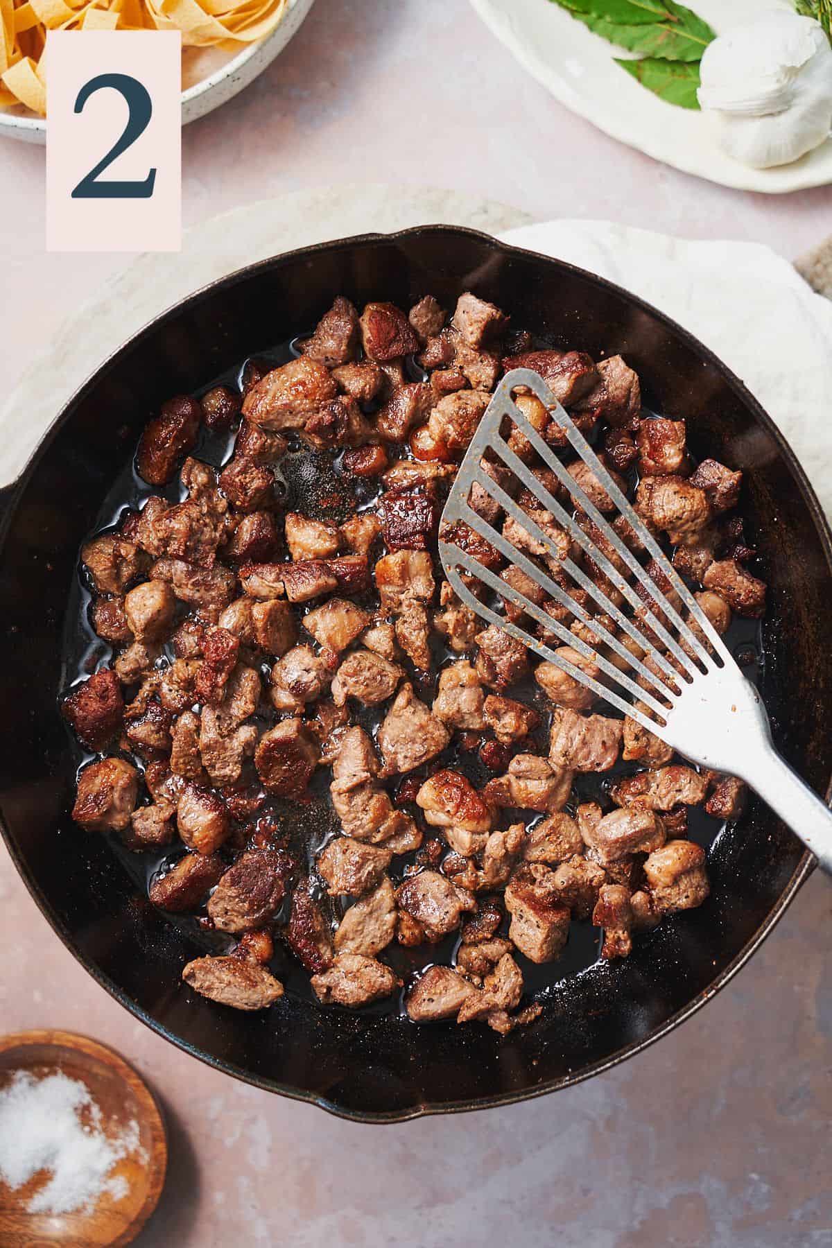 Cooked chunks of lamb in a cast iron skillet. 