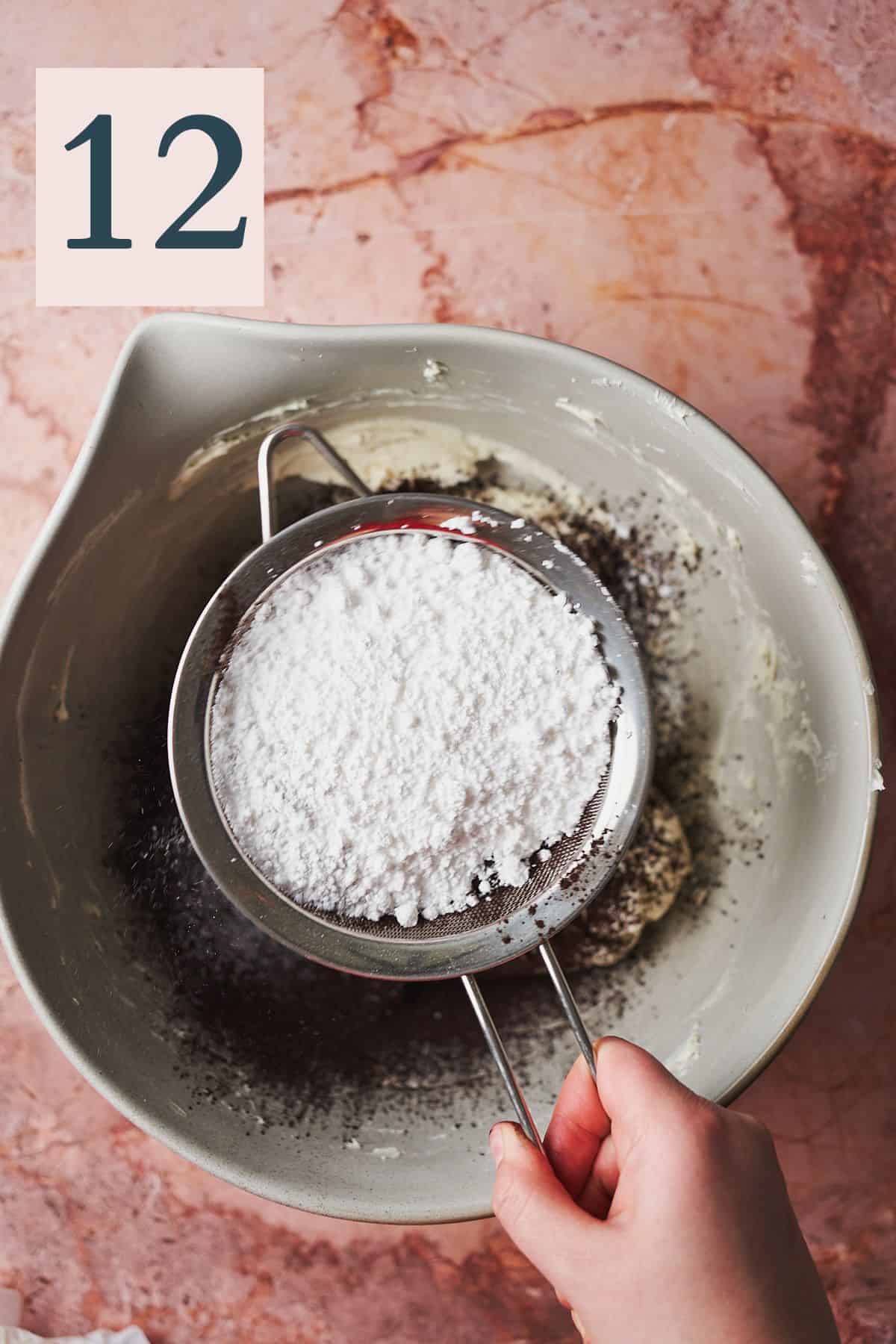 hand sifting powdered sugar into a bowl of frosting. 