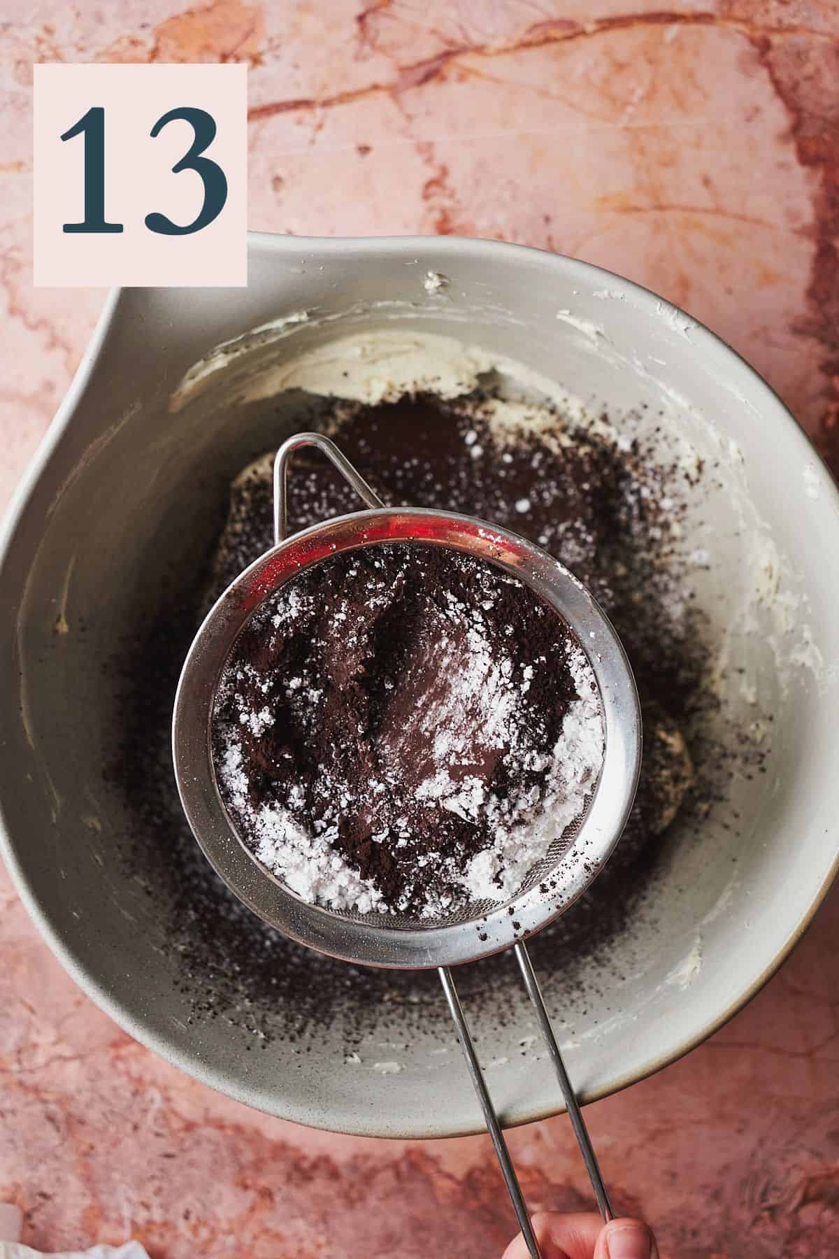hand sifting powdered sugar and black cocoa powder into a bowl of cream cheese frosting. 